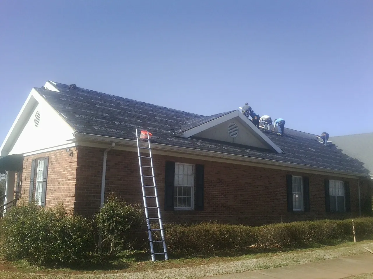 Crew tearing shingles off a brick ranch roof with a ladder set — Metal Roof Repair work by our crew in Geyserville