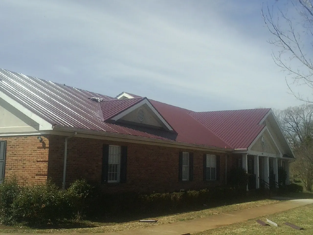 Red metal roof with gabled entries on a long brick building, from a Hail Damage Roof Repair job in Geyserville