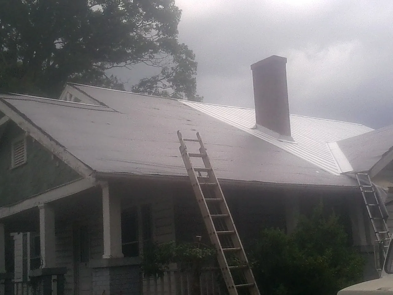 Ladders against a metal roof on an older home with a brick chimney in Geyserville