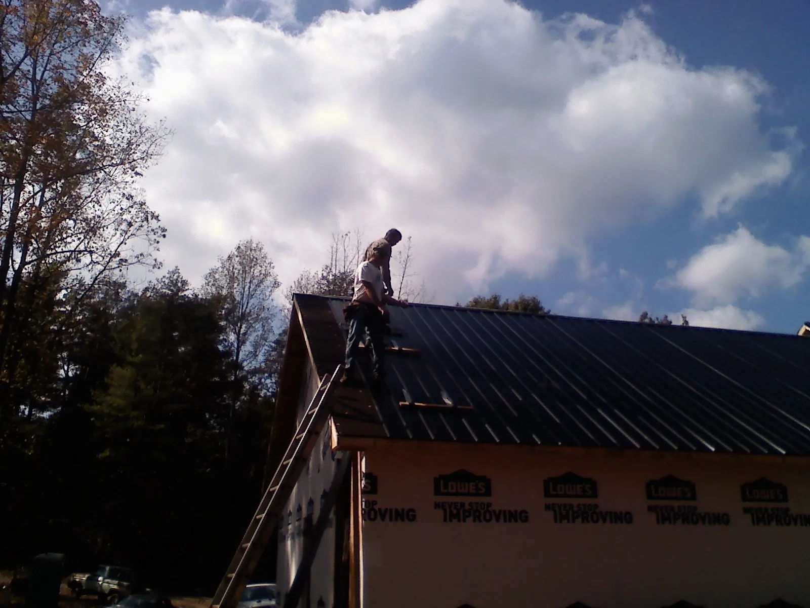 Roofer fastening dark metal panels high against a cloudy sky, from a Roof Inspection job in Geyserville